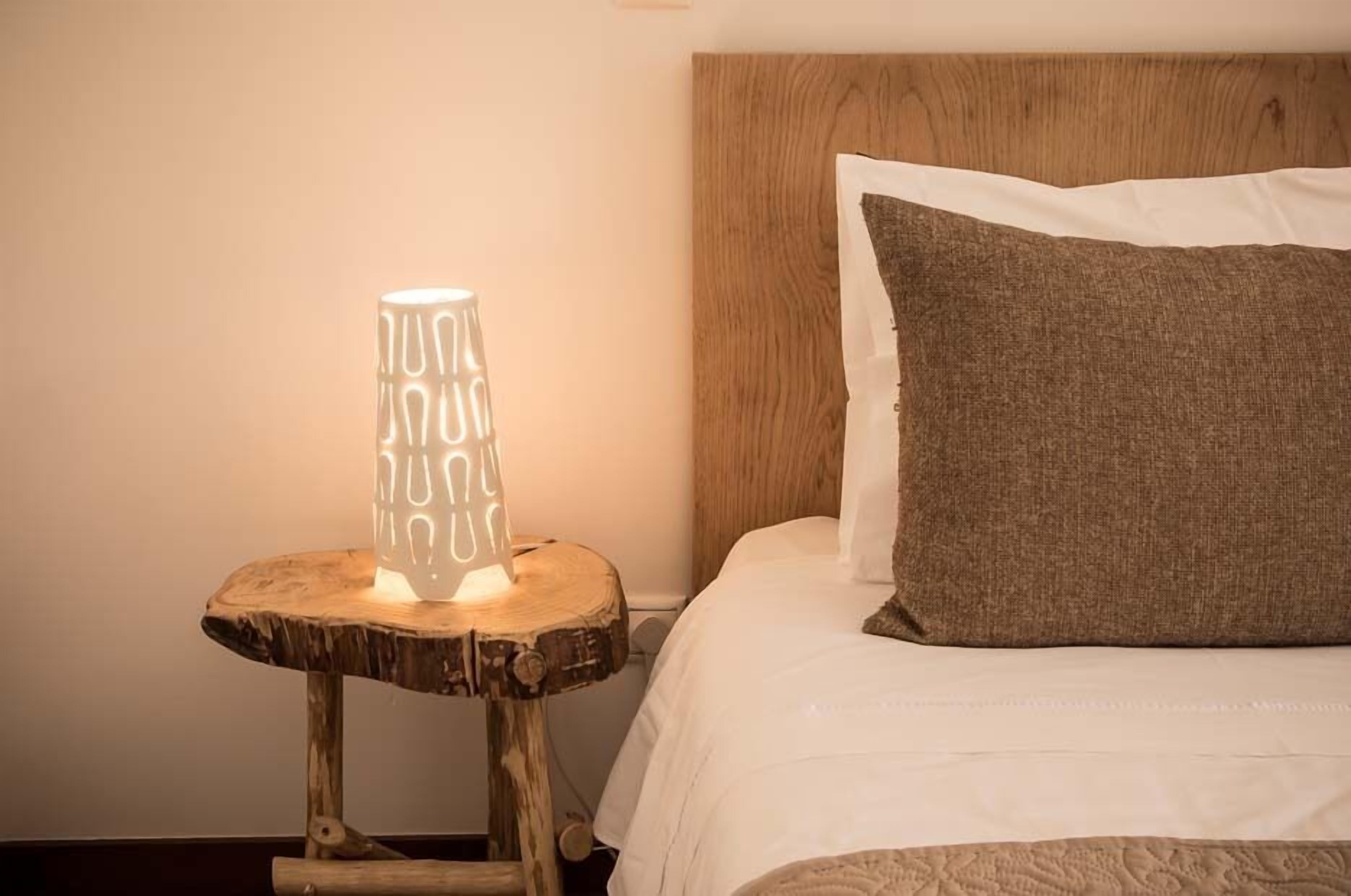 A bed with a wooden headboard, a bedside table with a textured lamp, and a brown pillow.