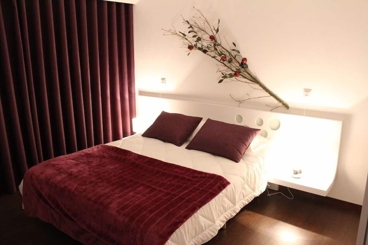 A neatly made bed with a white and maroon bedspread, two maroon pillows, and a maroon throw blanket. There is a decorative branch with red berries on the wall above the bed.