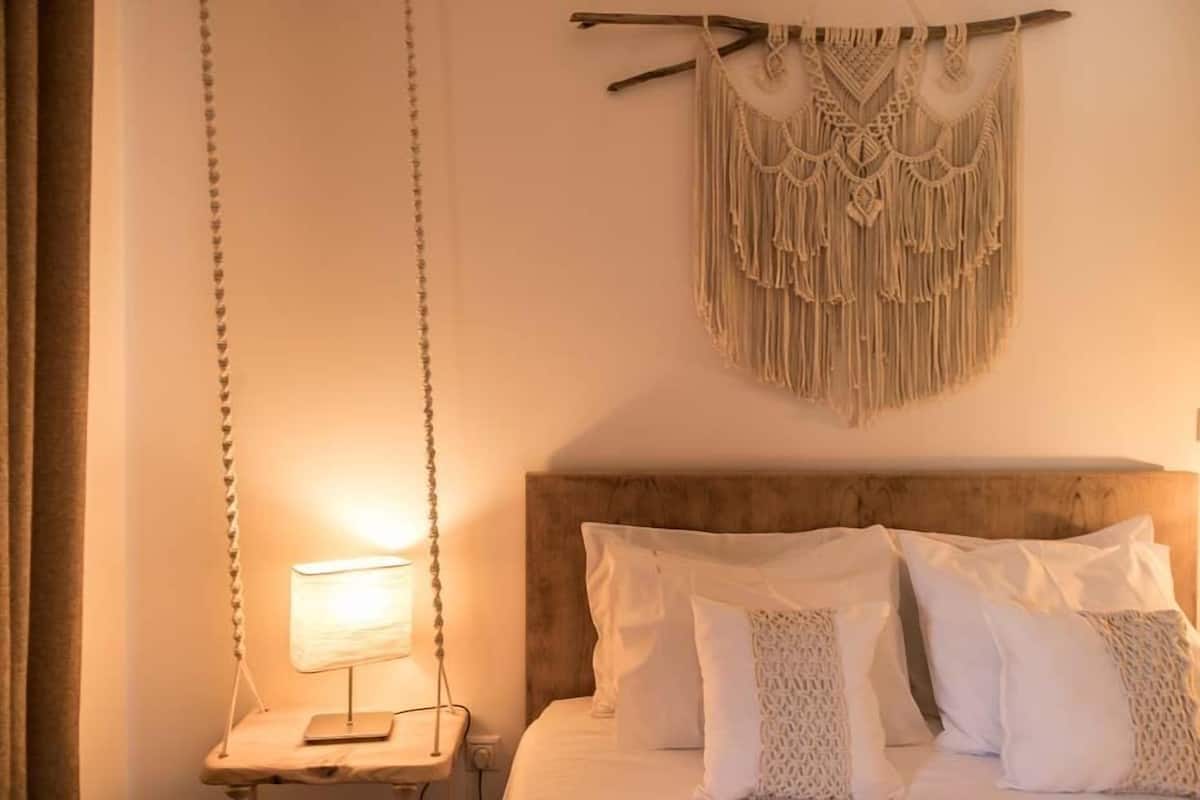 A bedroom with a bed, a bedside table with a lamp, and a macrame wall hanging.