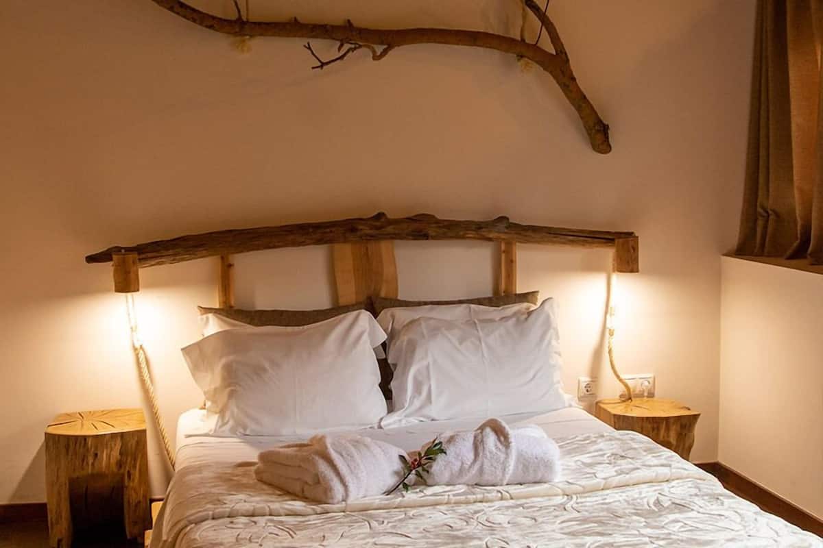 A bed with a wooden headboard, white linens, and a branch decoration. There are two nightstands with lamps.