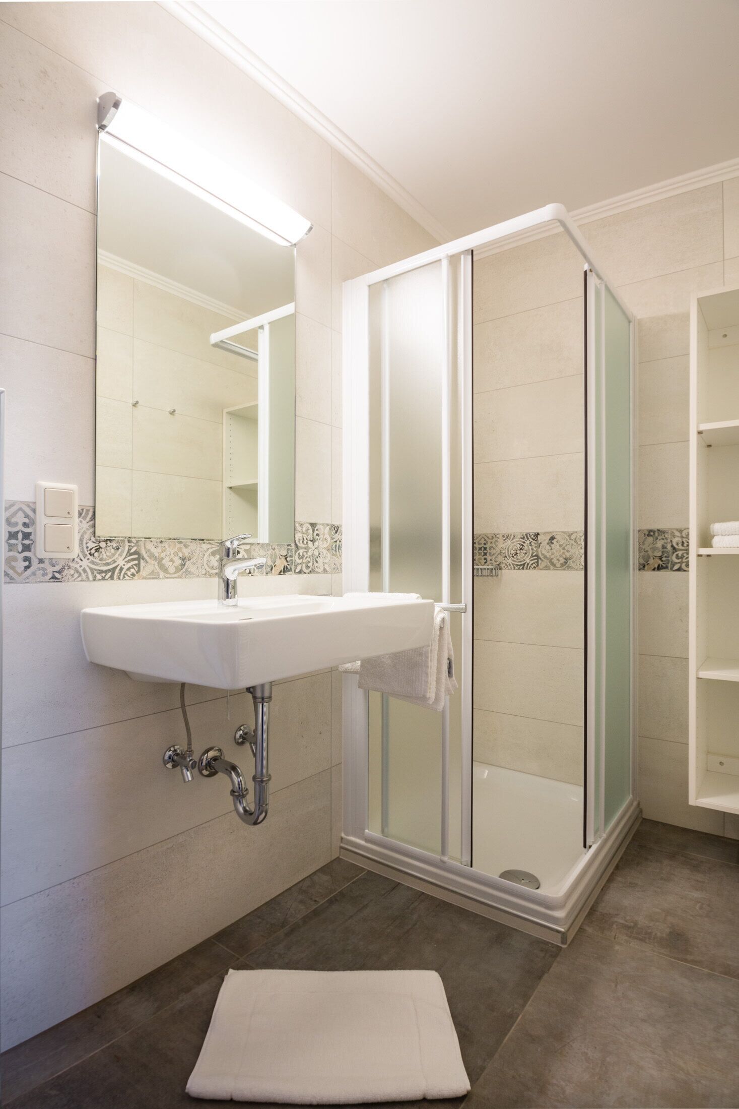 A bathroom with a white sink, a mirror, a glass shower enclosure, and a tiled shower area.