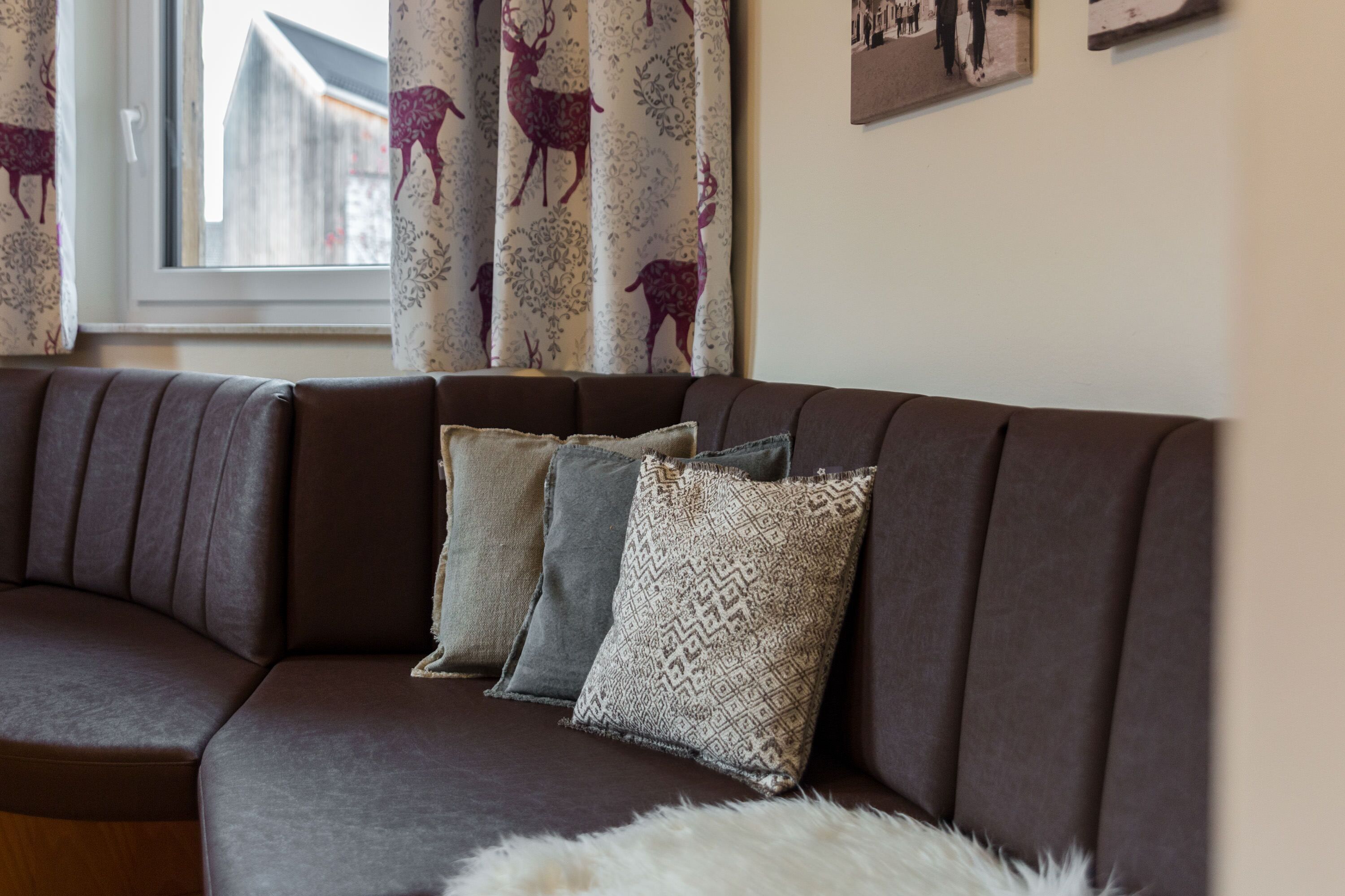 A brown sofa with patterned cushions in a room with a window and curtains with a deer pattern.