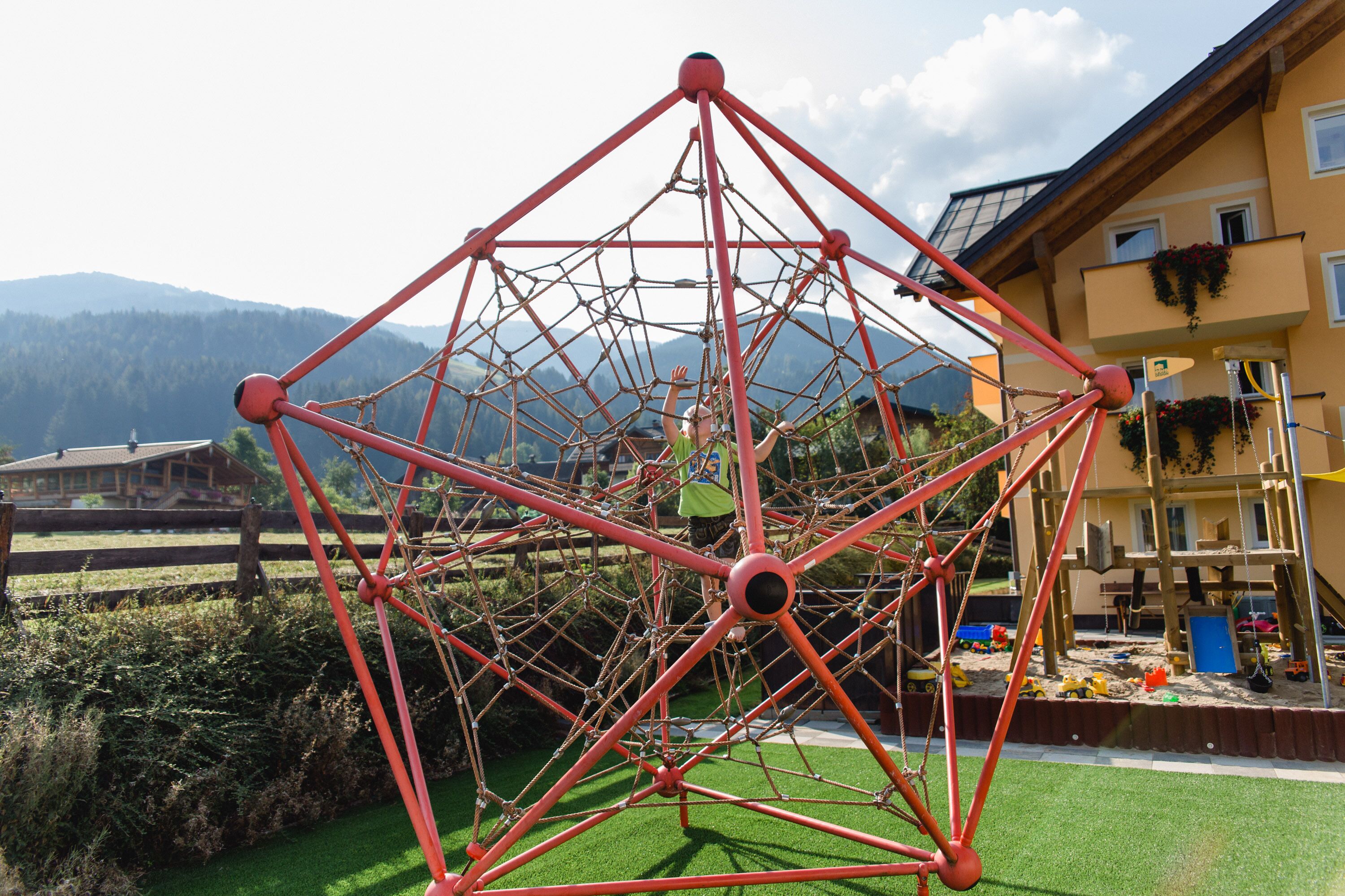 Estructura de juegos con diseño geométrico, rodeada por una cerca de madera y vegetación.