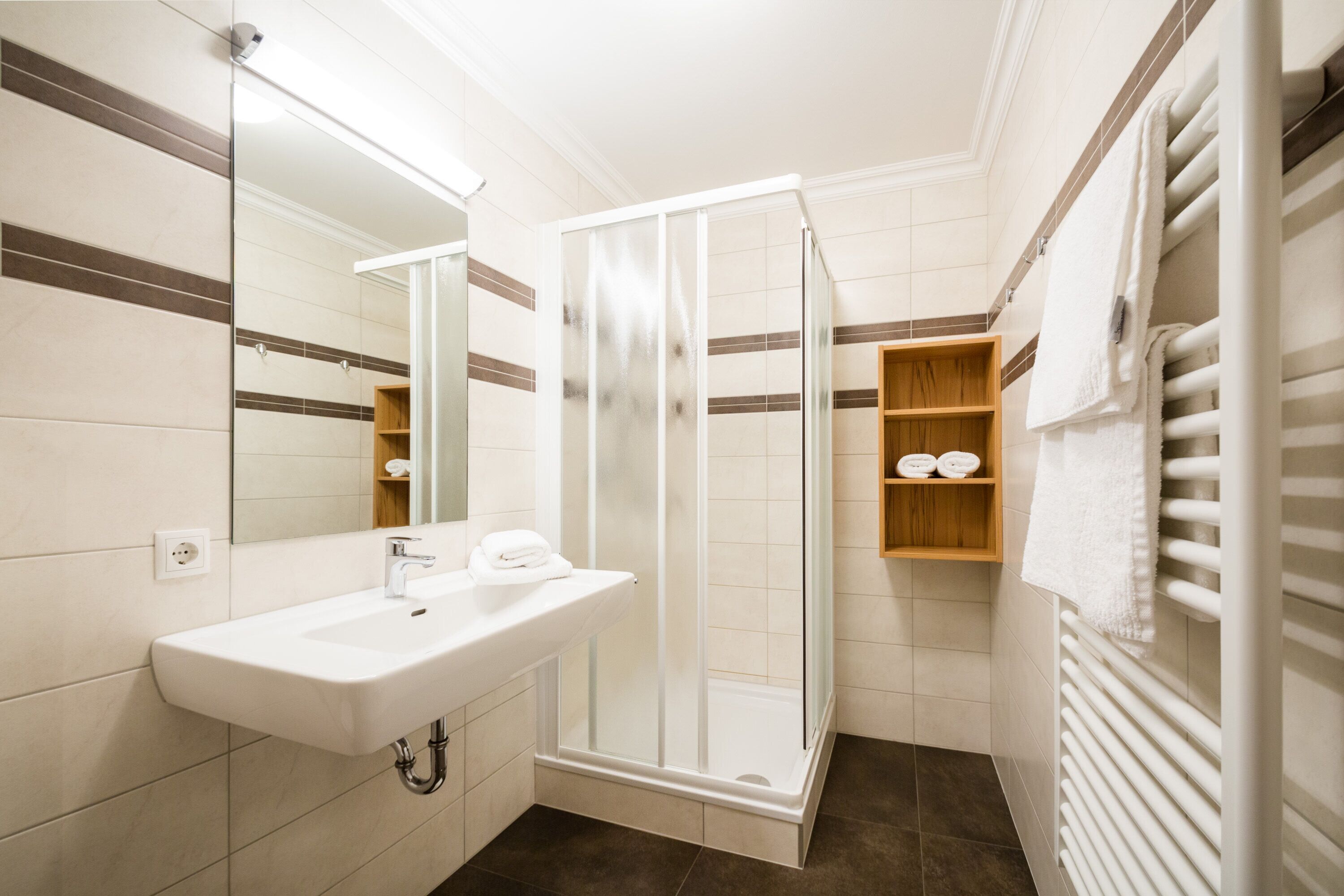 Bany amb un lavabo blanc, una cabina de dutxa de vidre i un suport per a tovalloles.