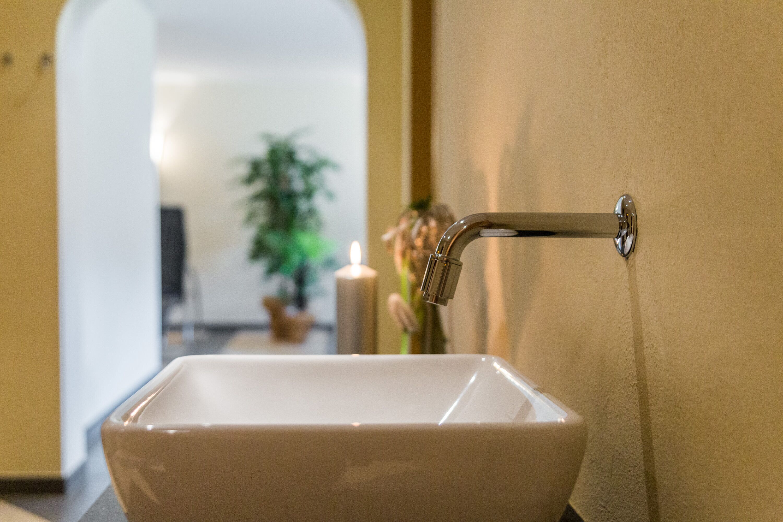 Un baño con un lavamanos blanco, un espejo y una planta al fondo.