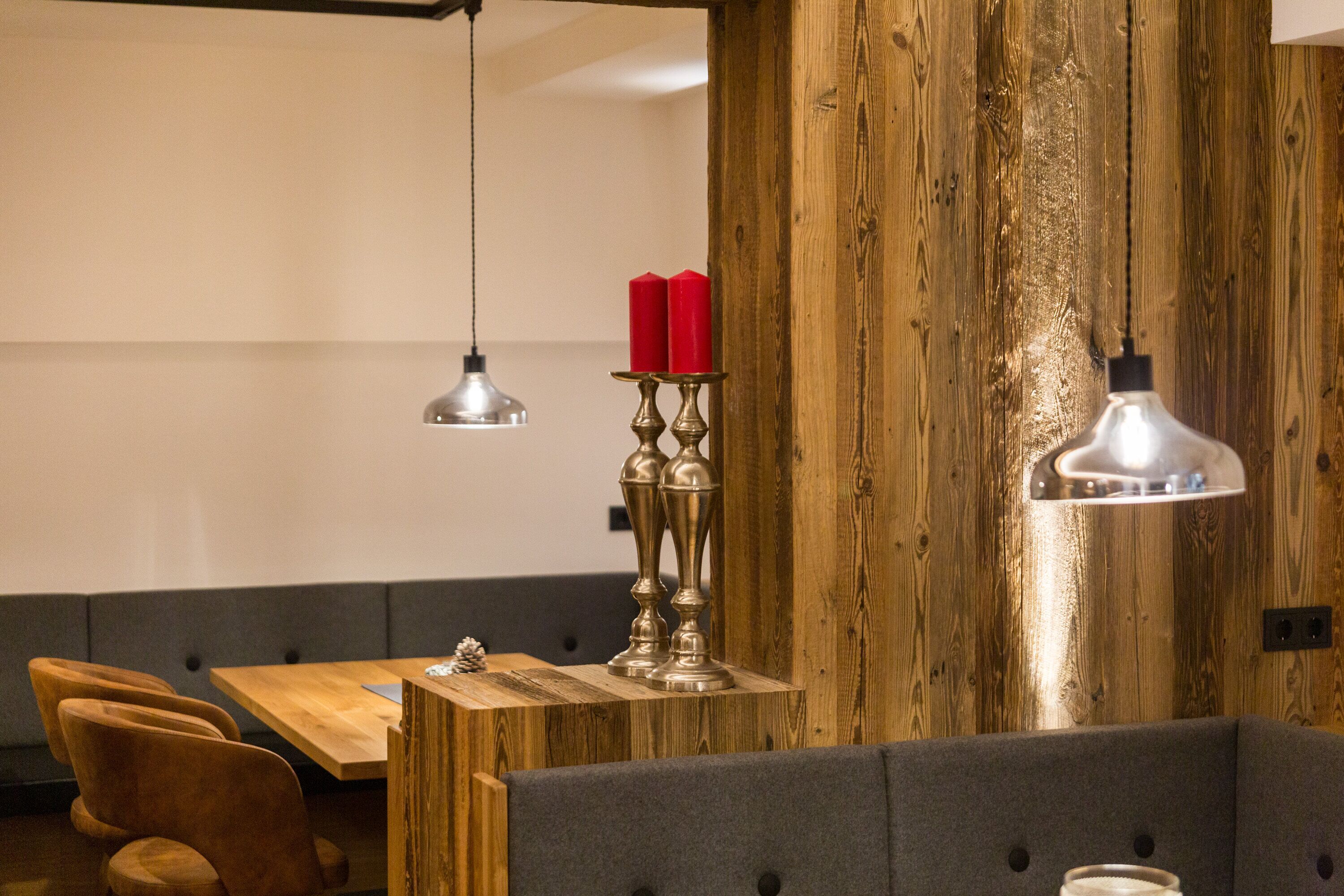 A wooden wall with a candle holder and two red candles, a wooden table with a metal lamp, and a gray upholstered bench.