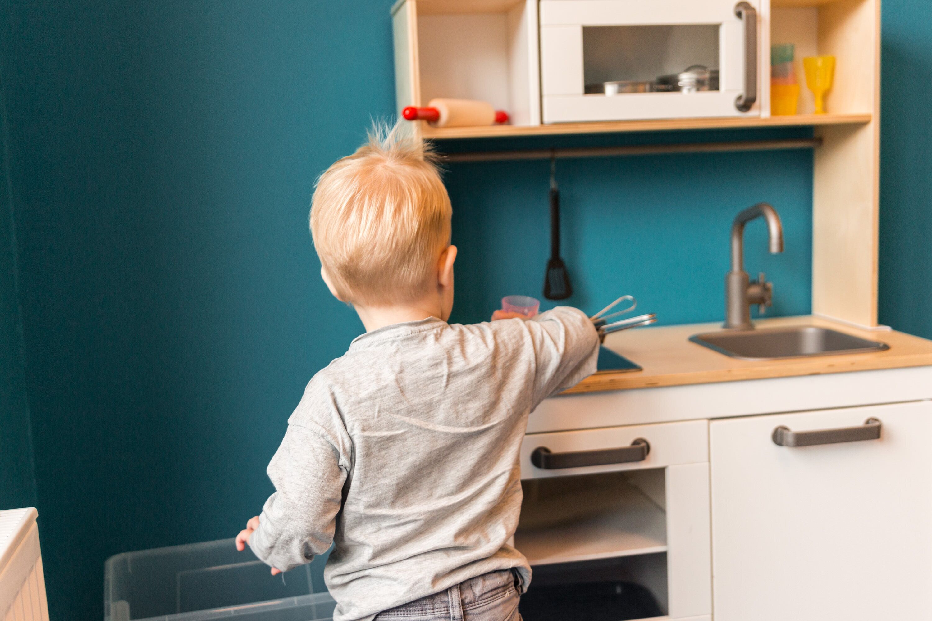 A child in a kitchen with a sink, cabinets, and a microwave.