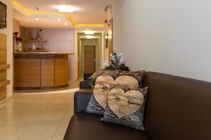 Un moderno vestíbulo de hotel con una mesa de recepción, un sofá con cojines con forma de corazón y un pasillo que conduce a una puerta.