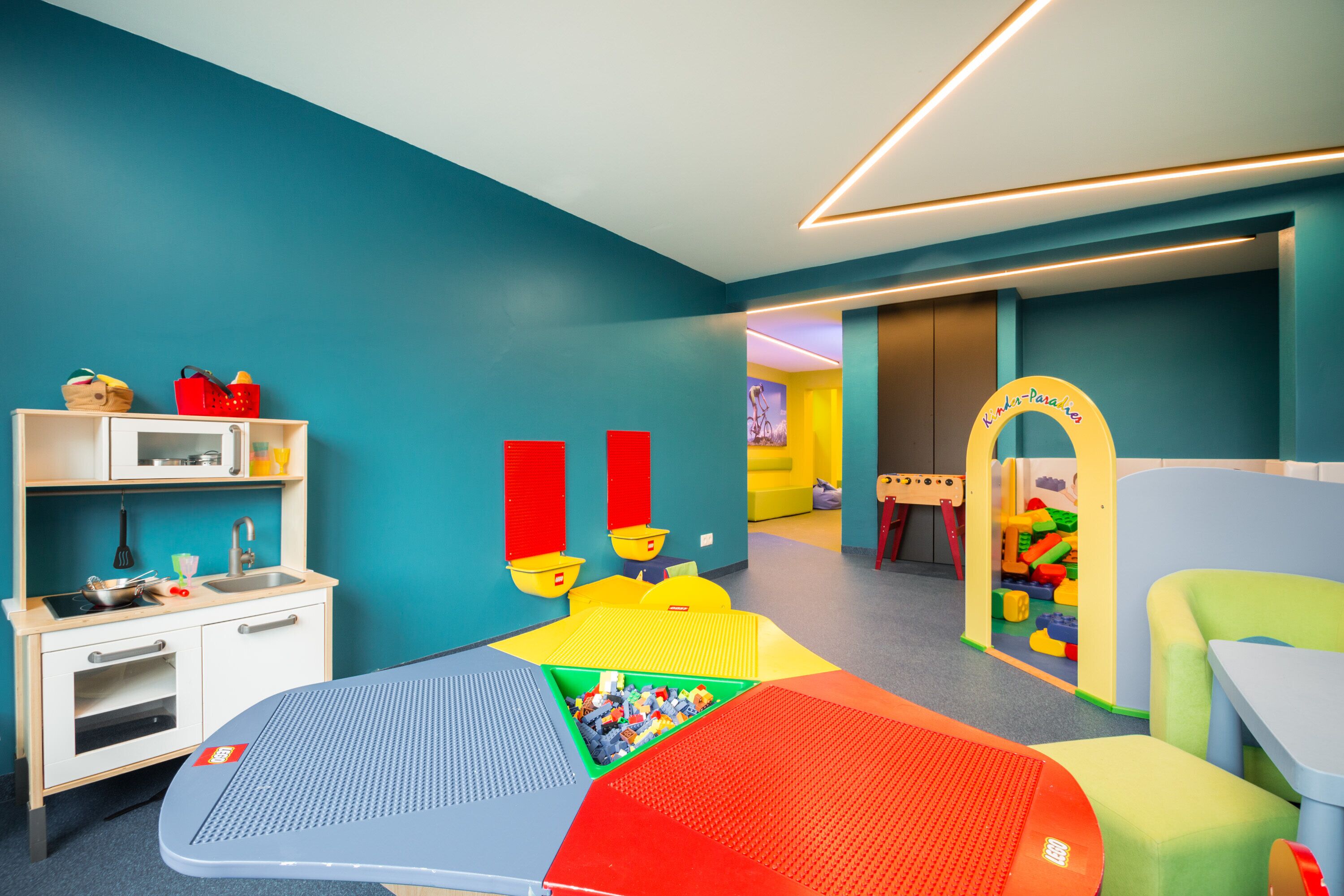 Un espace de jeux pour enfants avec un coin cuisine, des tapis de jeu colorés et une maison de jeu.