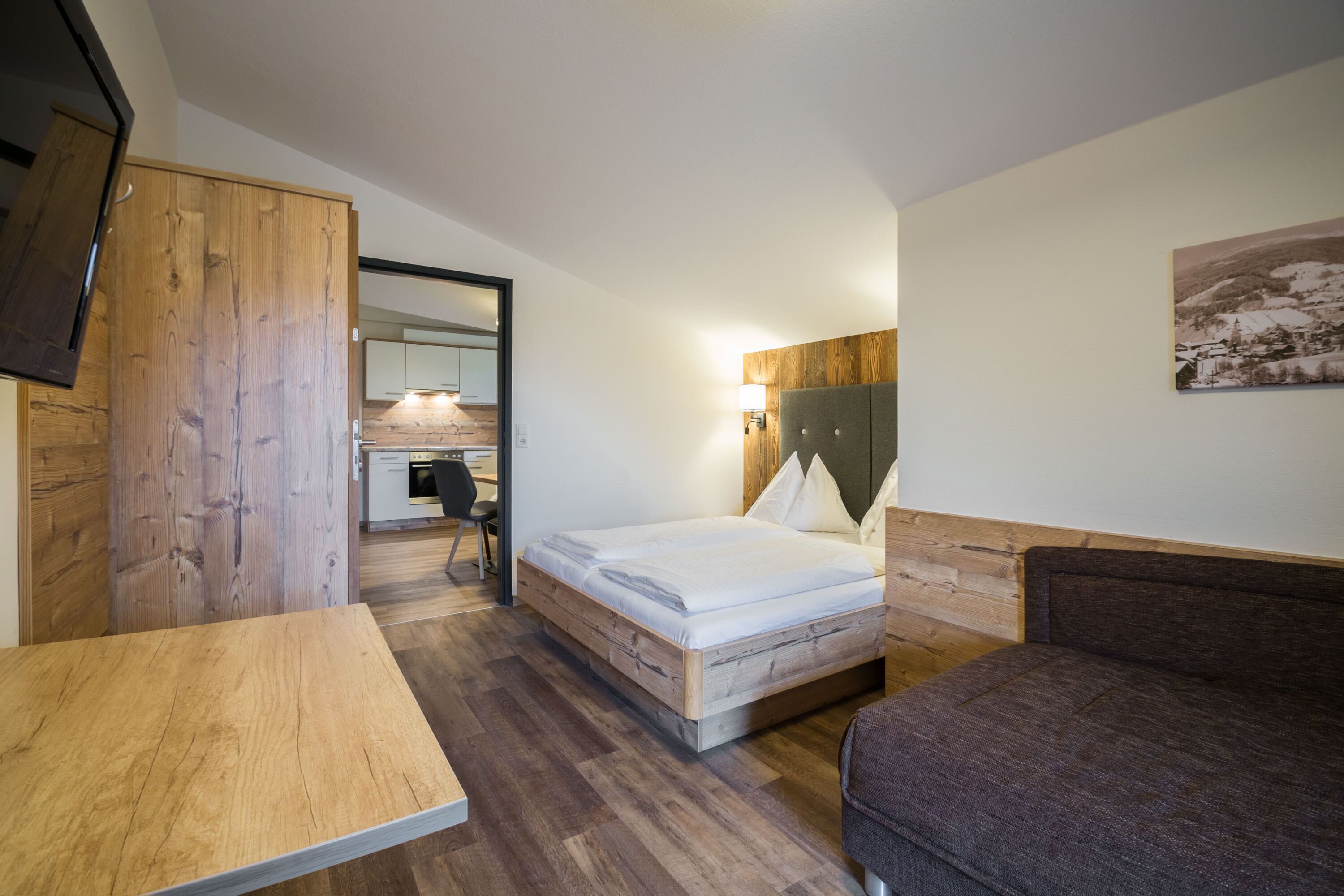 A bedroom with a wooden bed, a small table, a sofa, and a desk with a chair.