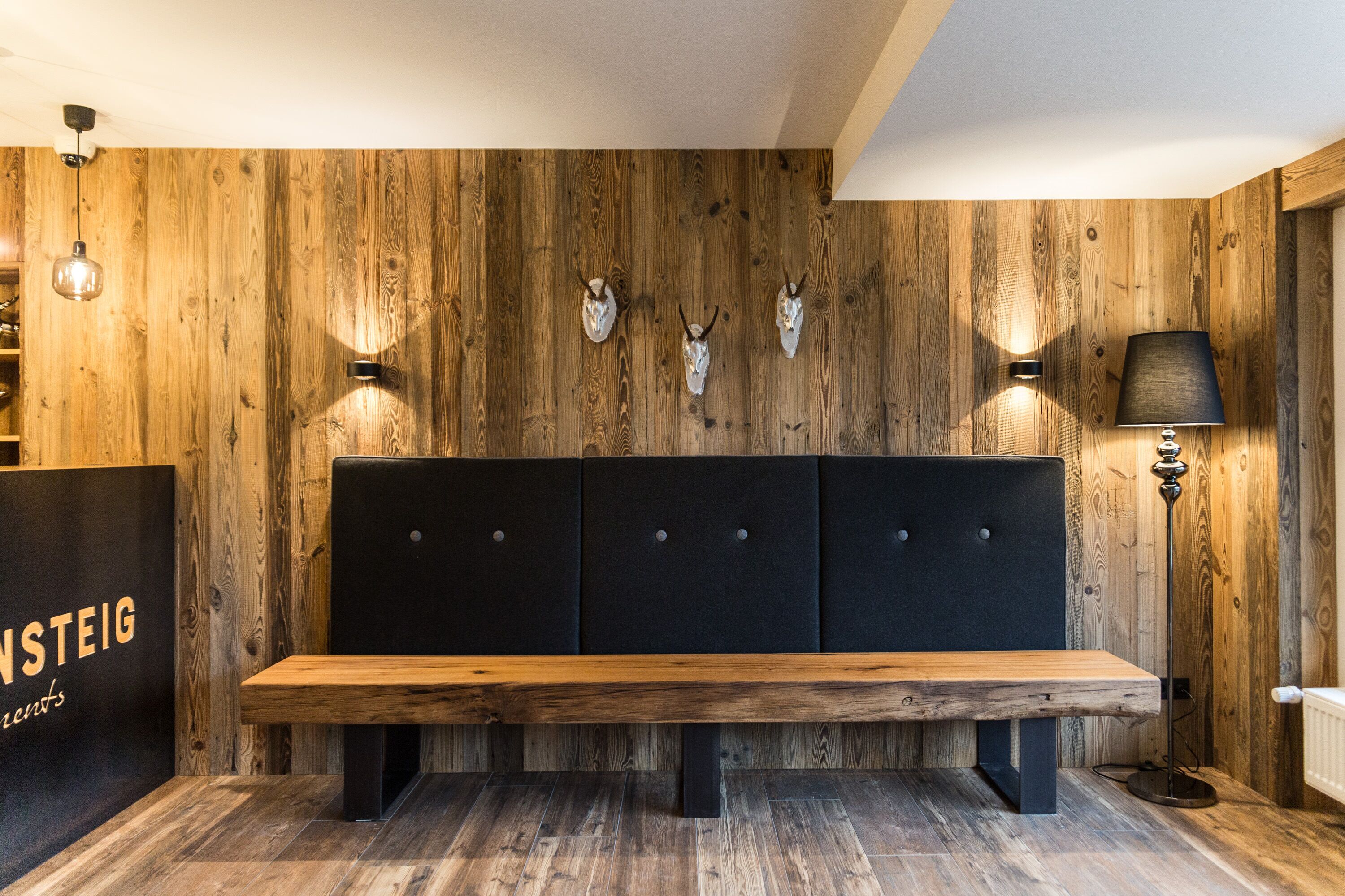 A wooden wall with three skull decorations, a bench, and a lamp.