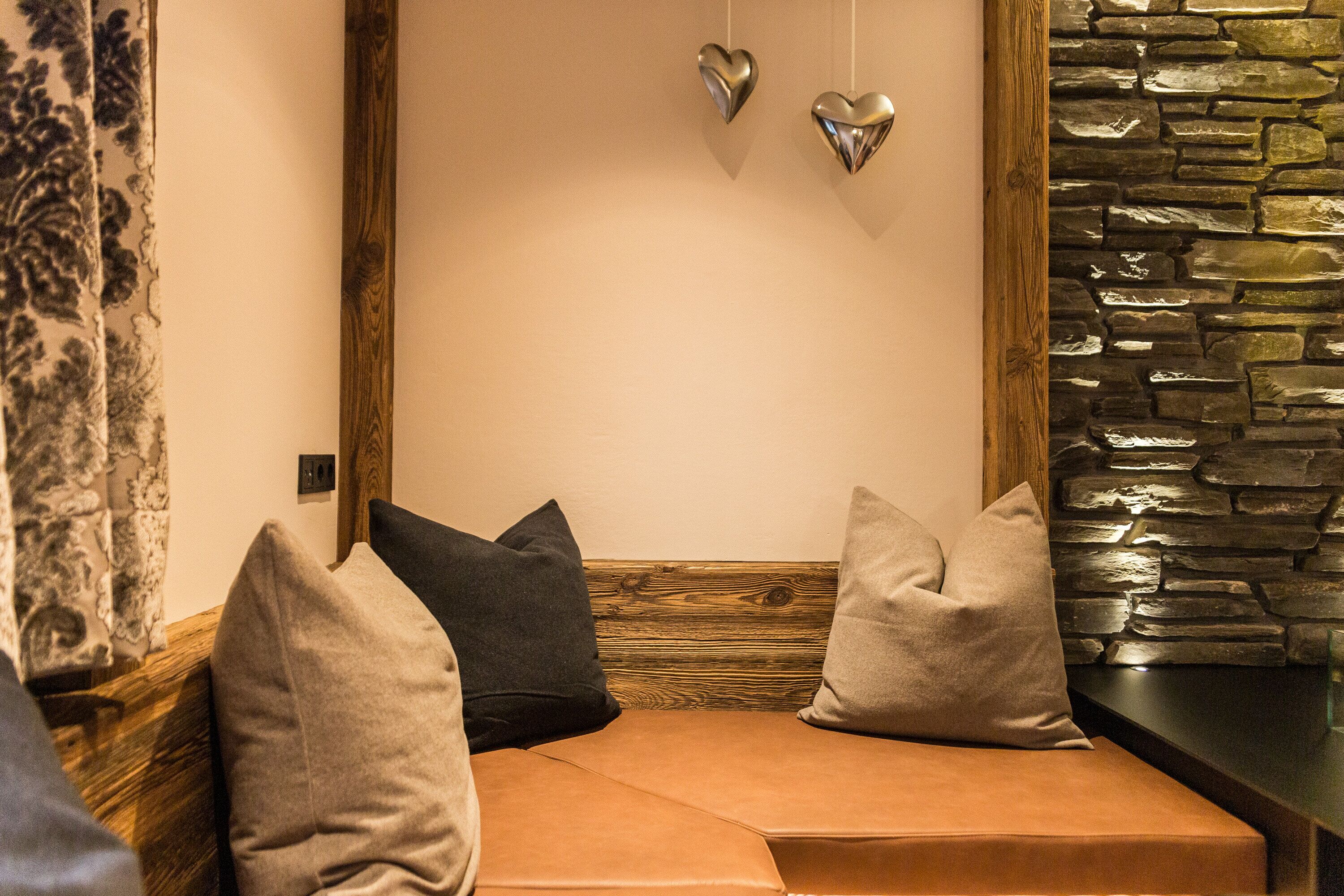 A cozy seating area with a cushioned bench, wooden beams, and a stone wall.