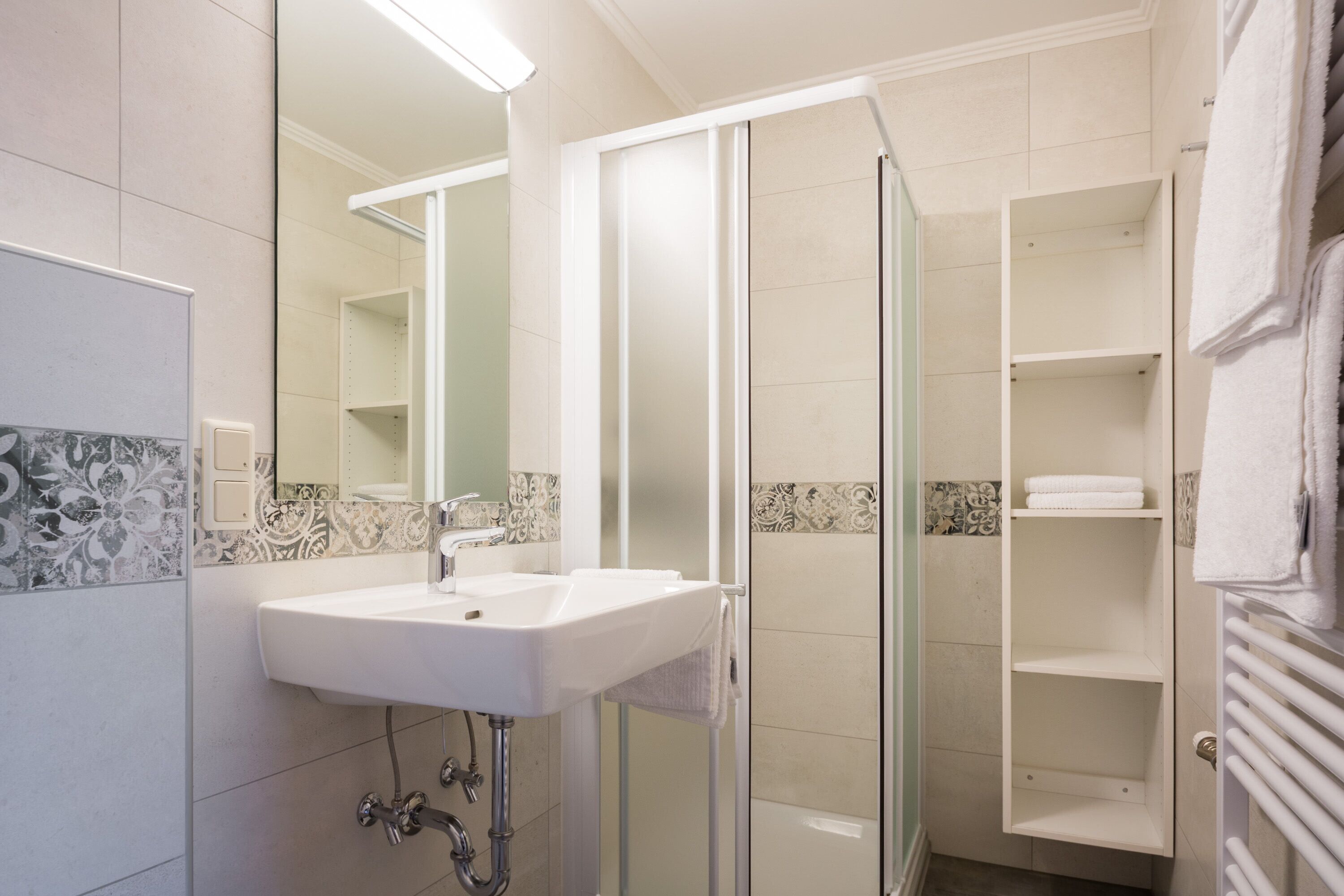 A bathroom with a white sink, a glass shower enclosure, and a tiled wall with a decorative border.