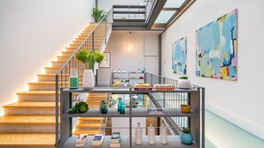 A modern staircase with a glass railing, a metal shelf with decorative items, and abstract paintings on the wall. - Canto de Luz (Porto)