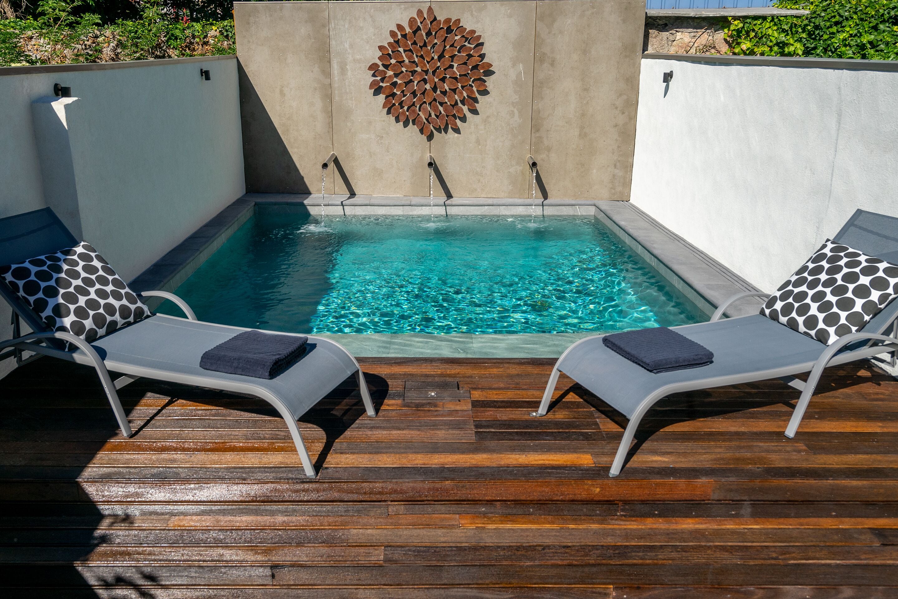 Een klein, rechthoekig jacuzzi met een houten terras en twee loungestoelen met gestreepte kussens.