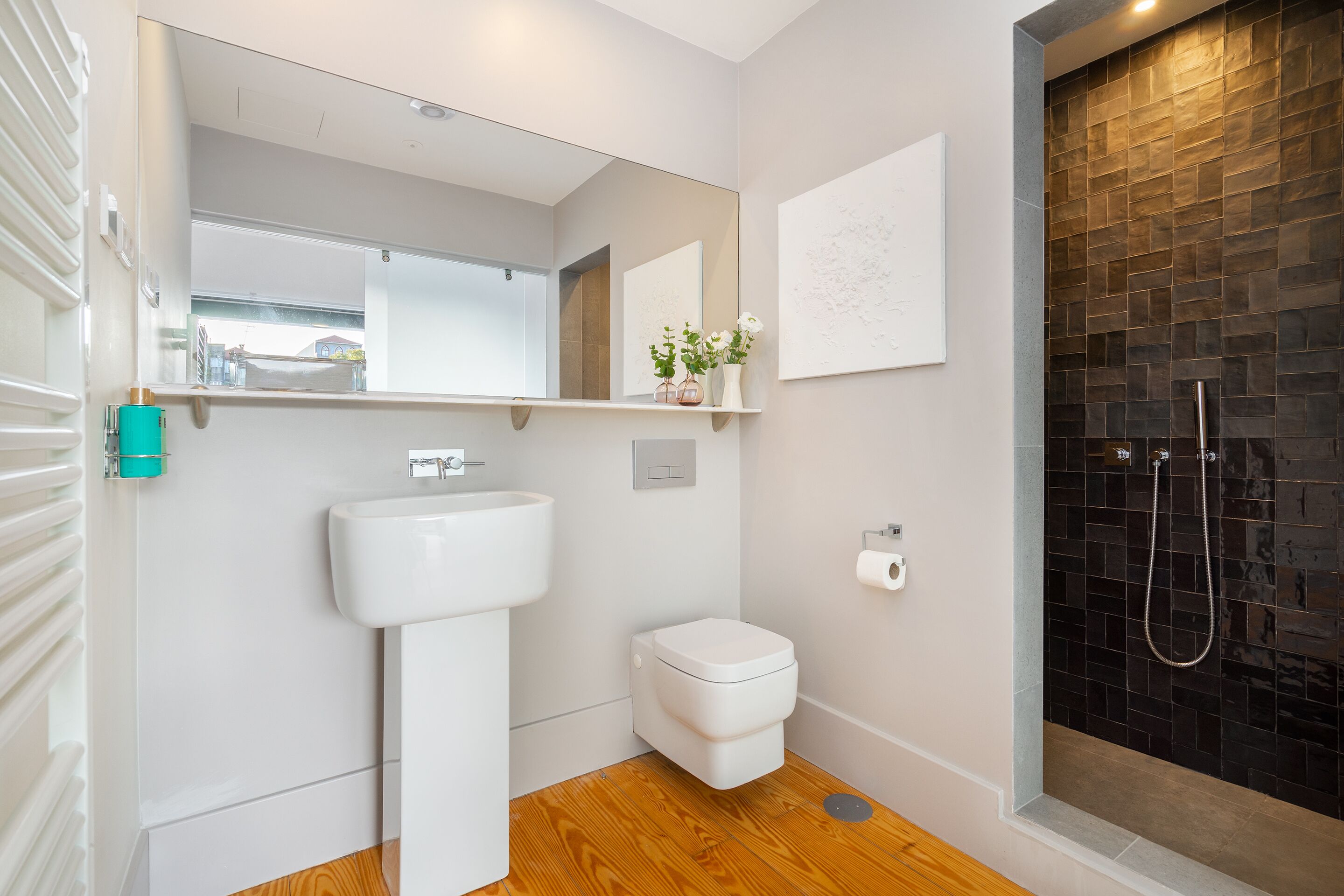 A modern bathroom with a white sink, a toilet, and a shower area with a dark tiled wall.