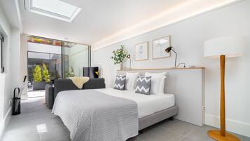 A modern bedroom with a large bed, bedside tables, a floor lamp, and a view of a balcony with plants.
