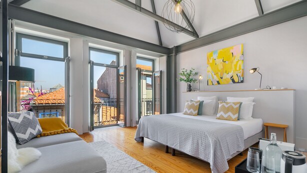 A modern bedroom with a large bed, a sofa, and a view of the city through large windows. - Canto de Luz (Porto)