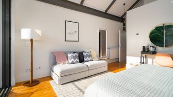 Quarto moderno com cama, sofá, luminária de chão e espelho redondo.