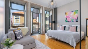 A modern bedroom with a large bed, a sofa, and a view through open doors to an outdoor balcony. - Canto de Luz (Porto)