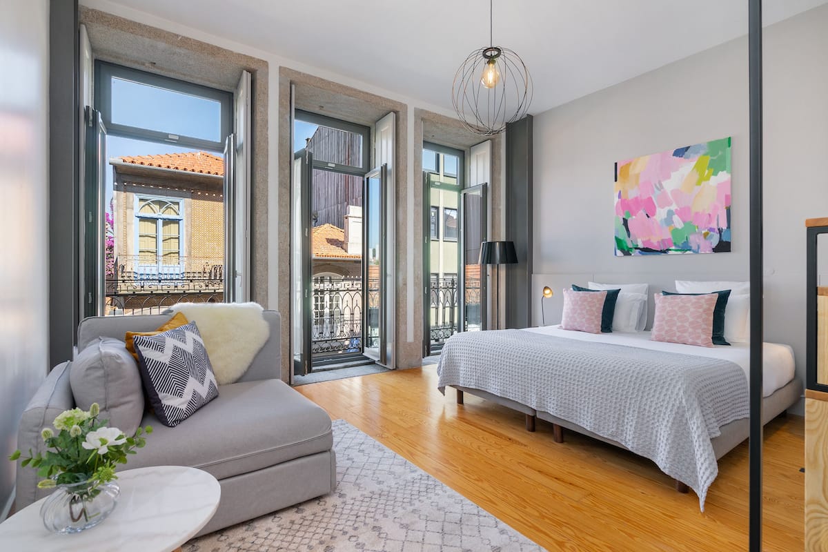 A modern bedroom with a large bed, a sofa, and a view through open doors to an outdoor balcony.