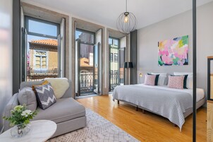 A modern bedroom with a large bed, a sofa, and a view through open doors to an outdoor balcony.