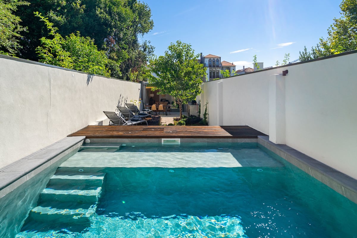 A swimming pool with a wooden deck, surrounded by white walls and trees.