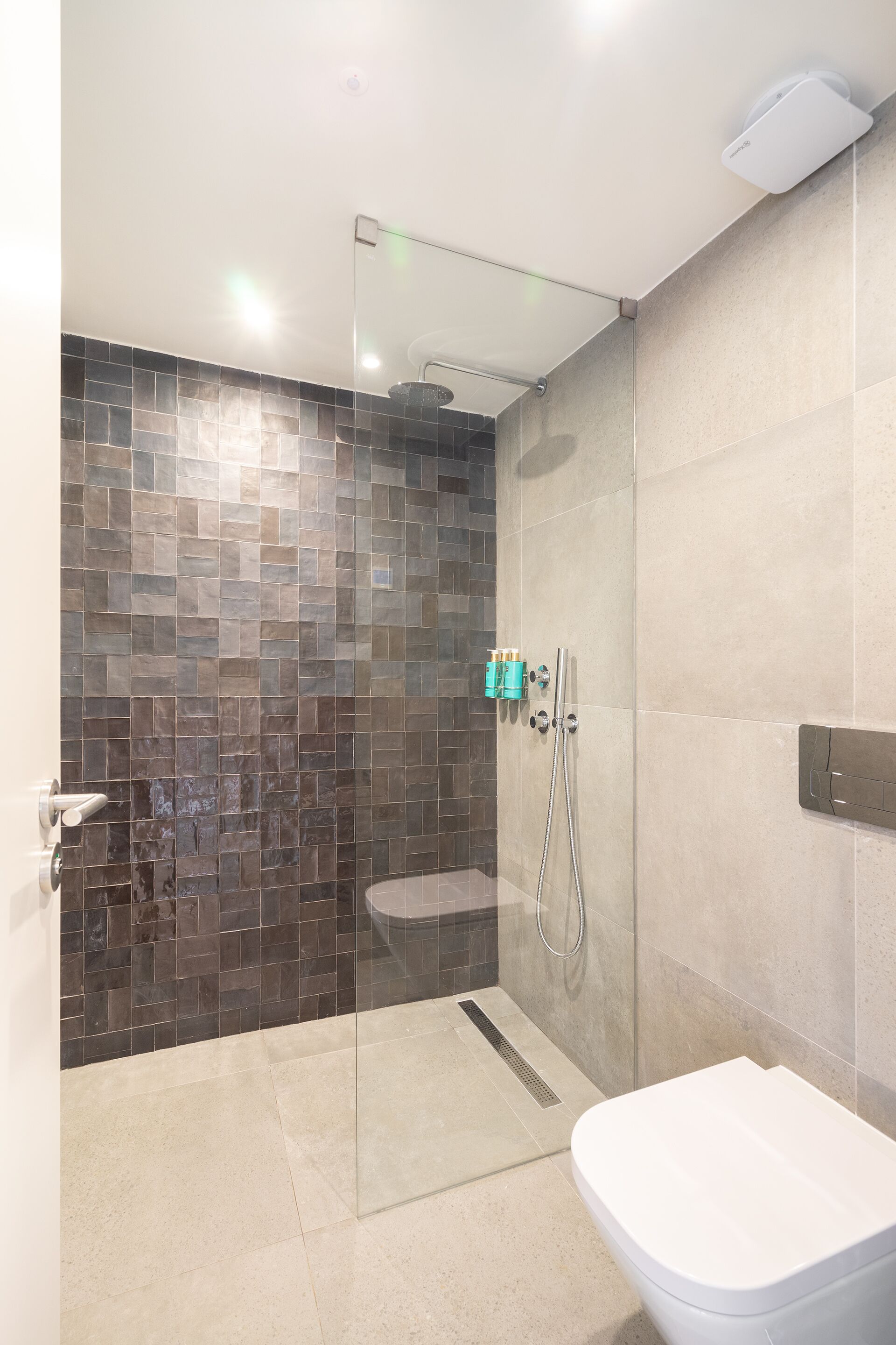A modern bathroom with a glass-enclosed shower, a white toilet, and a tiled wall with a mix of brown and beige tiles.