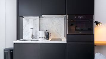 A modern kitchen with dark cabinetry, a marble countertop, a coffee maker, and a built-in oven.