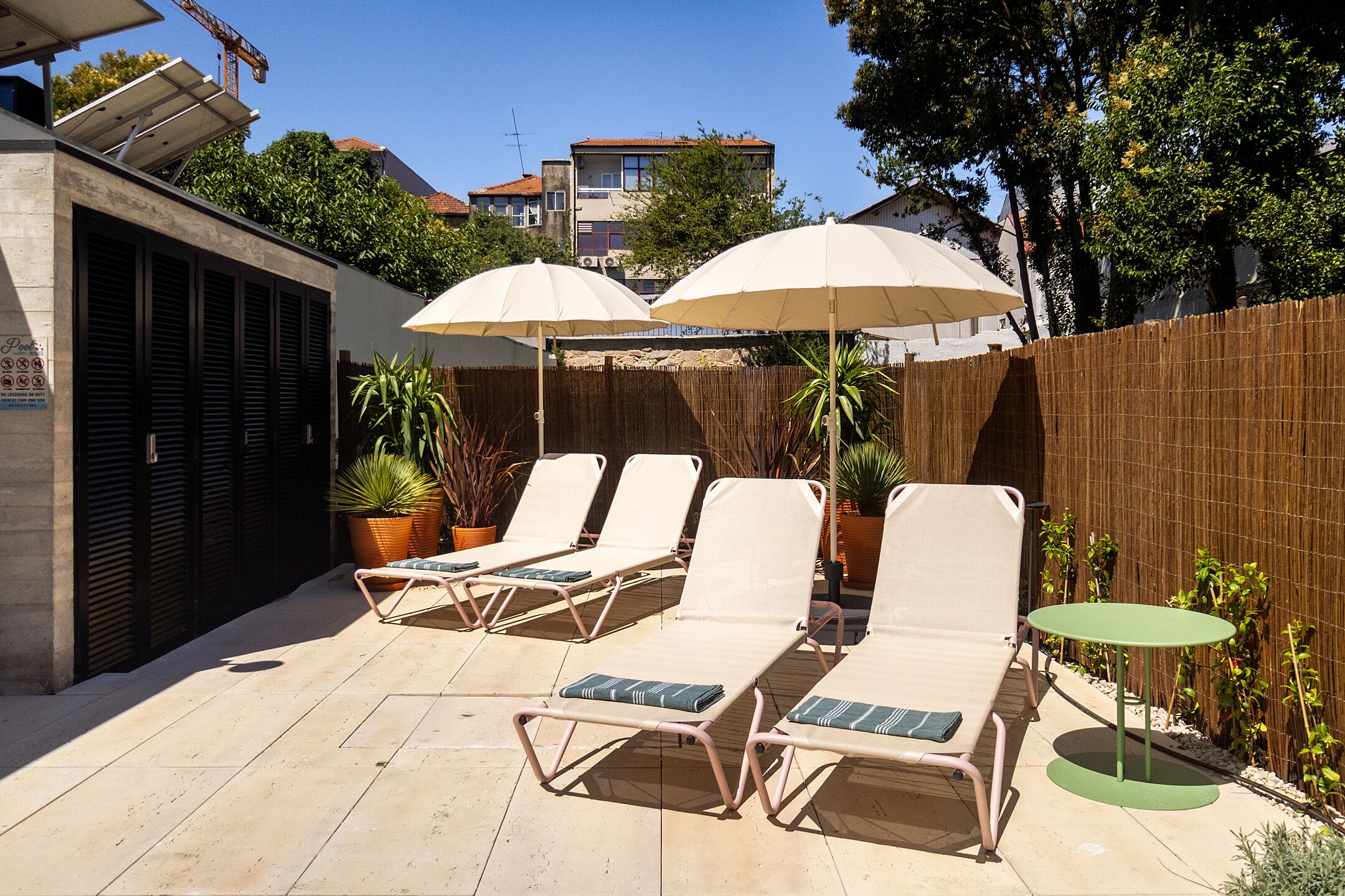 A patio with four lounge chairs and two umbrellas, surrounded by a wooden fence and potted plants.