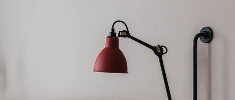 A bed with a wooden headboard, a red desk lamp, and a brown pillow.