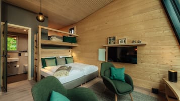 Ein modernes Schlafzimmer mit einem Bett, zwei grünen Sesseln, einem Fernseher und einer Holzzieldecke.