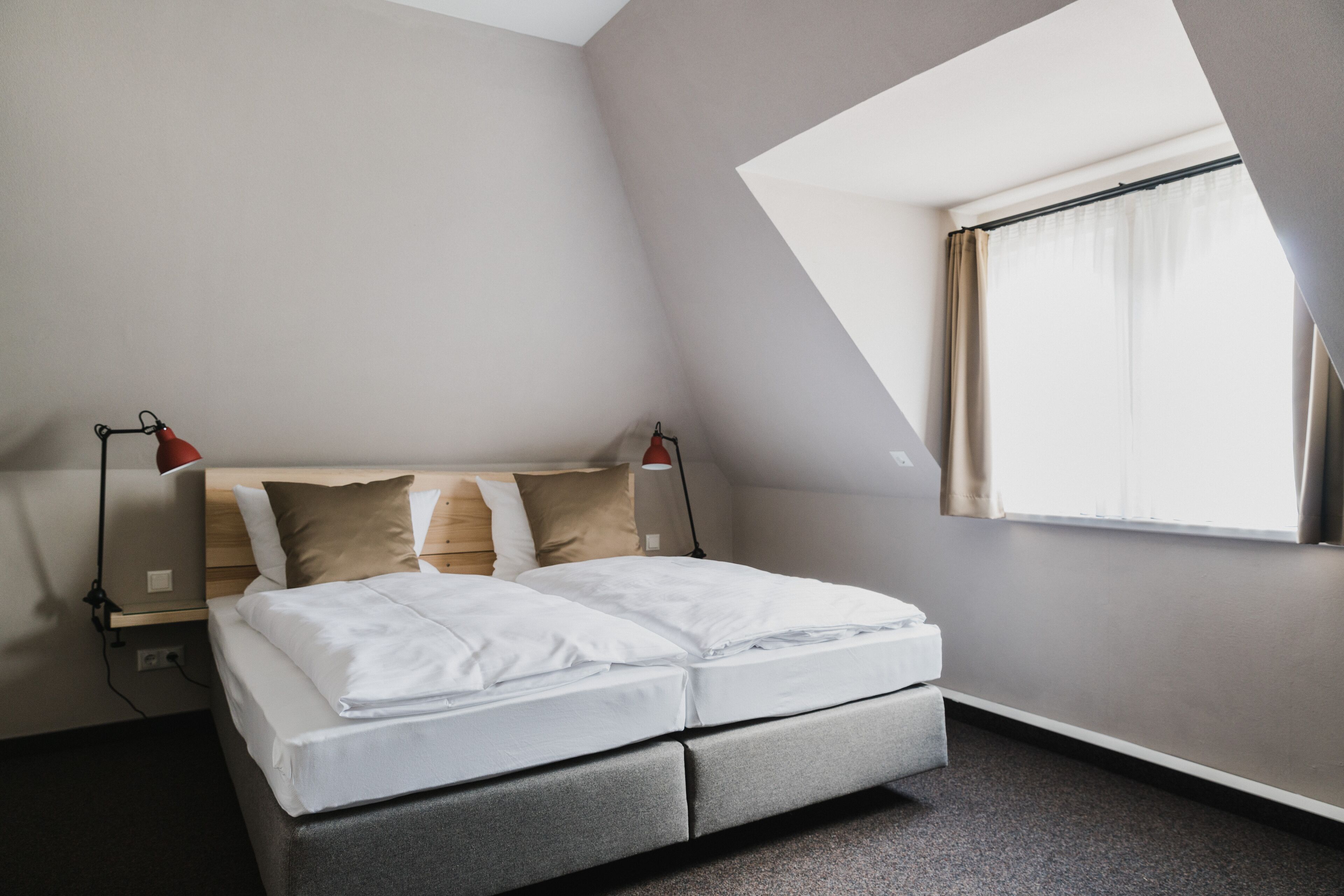 A modern bedroom with a bed, bedside lamps, and a window with curtains.