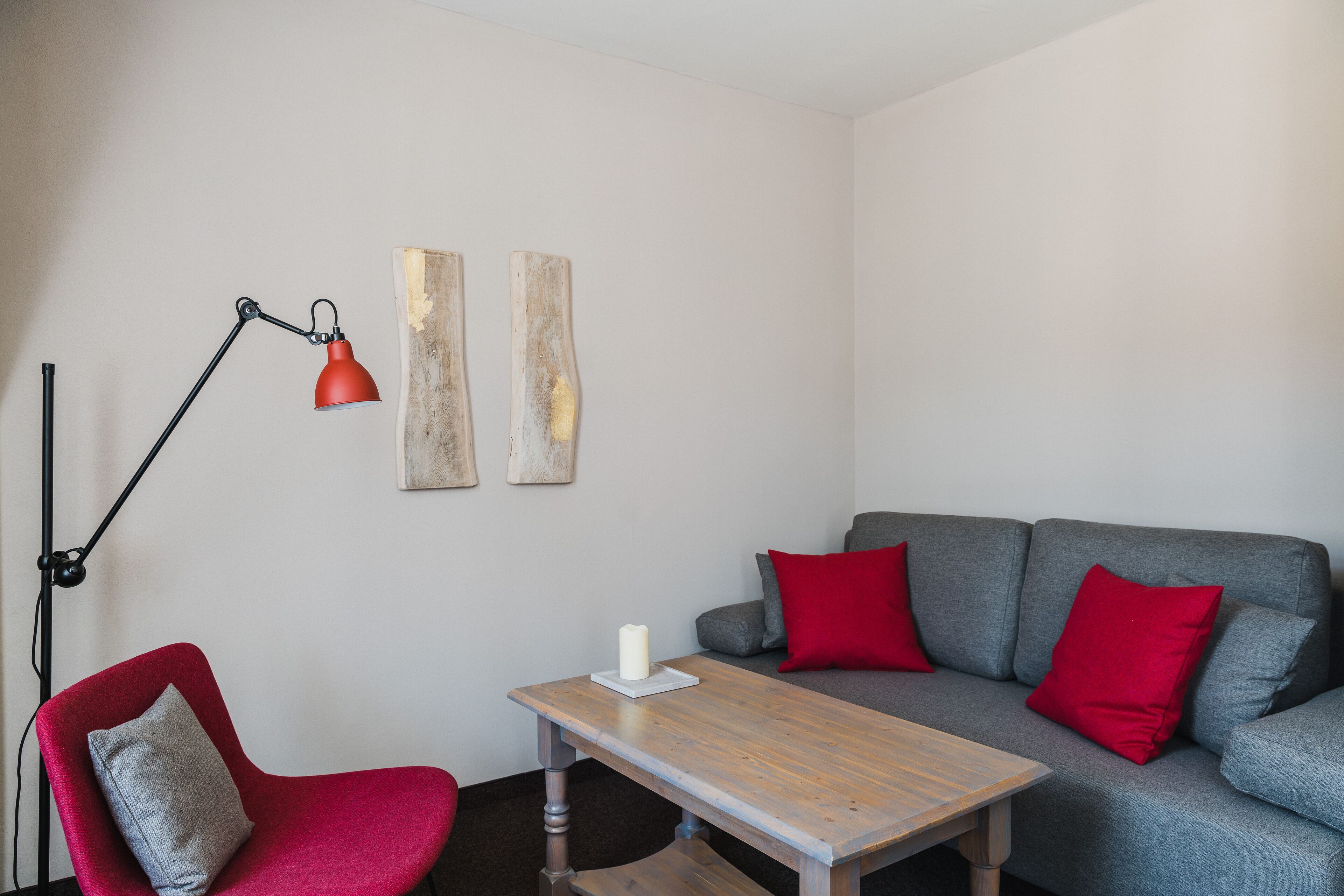 A modern living room with a grey sofa, red cushions, a red floor lamp, a wooden coffee table, and a red chair.