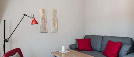 A modern living room with a grey sofa, red cushions, a red floor lamp, a wooden coffee table, and a red chair.