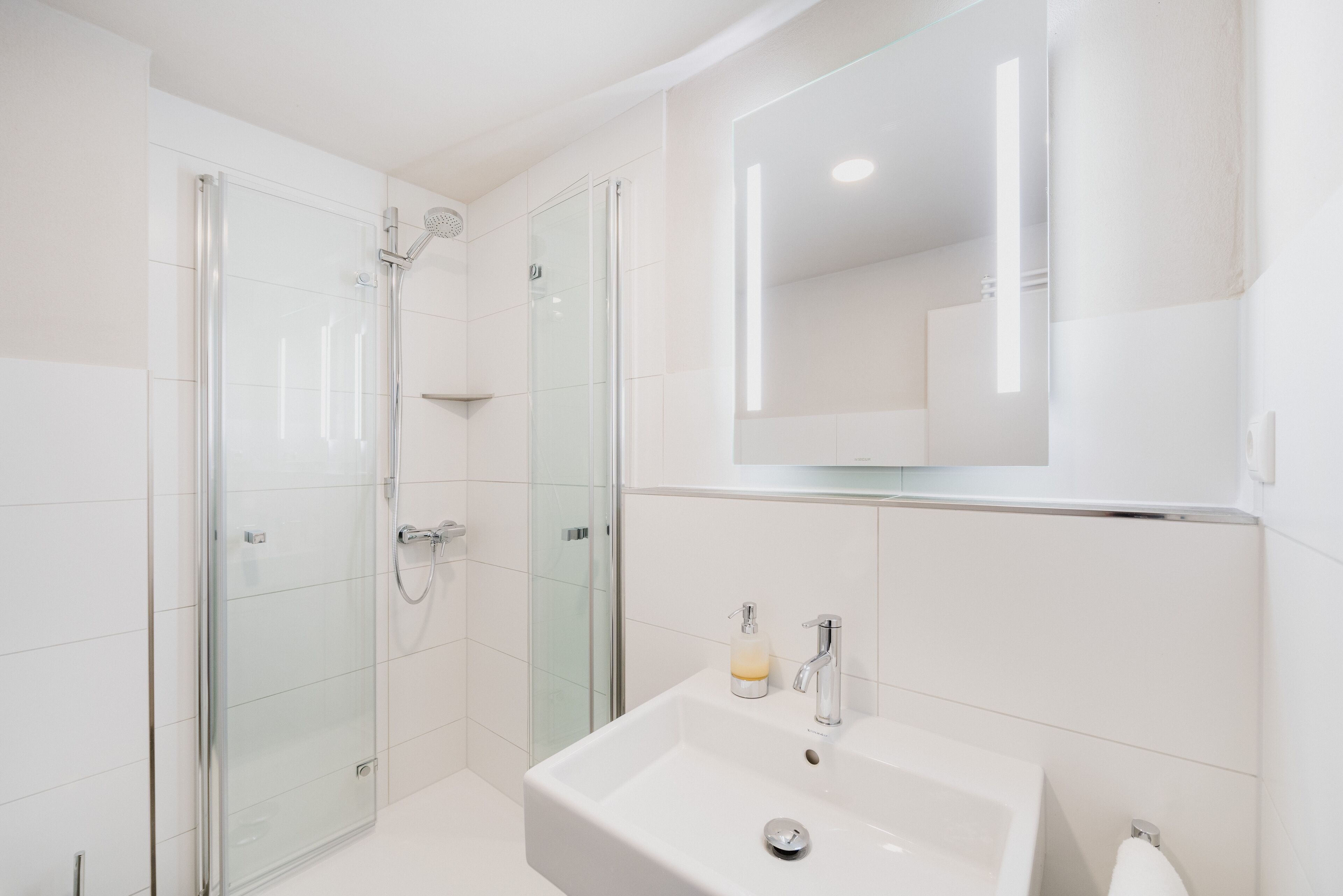 A modern bathroom with a glass-enclosed shower, a white sink, and a large mirror above the sink.