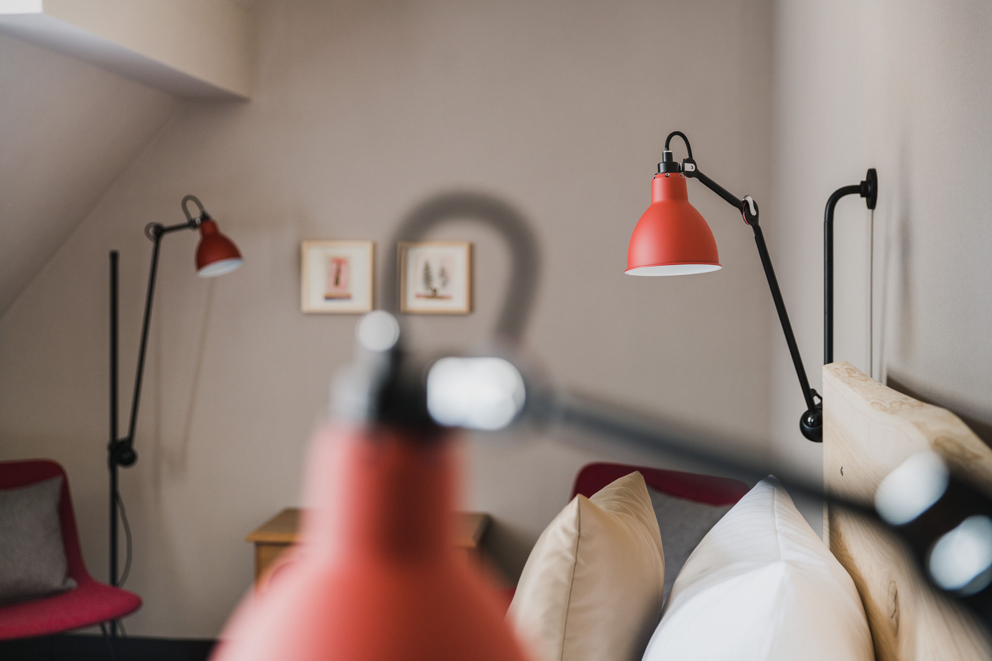 A room with a red desk lamp, a red chair, and a wooden headboard.