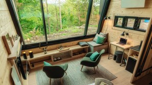 A cozy cabin interior with a large window offering a forest view, a seating area with a laptop, and a small kitchenette. - Hotel Villa Bodeblick (Wernigerode)
