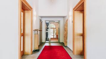 A hallway with wooden doors, a red carpet, and a staircase leading to an outdoor area.