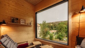 A wooden cabin with a large window, a sofa, a chair, and a small table. - Hotel Villa Bodeblick (Wernigerode)