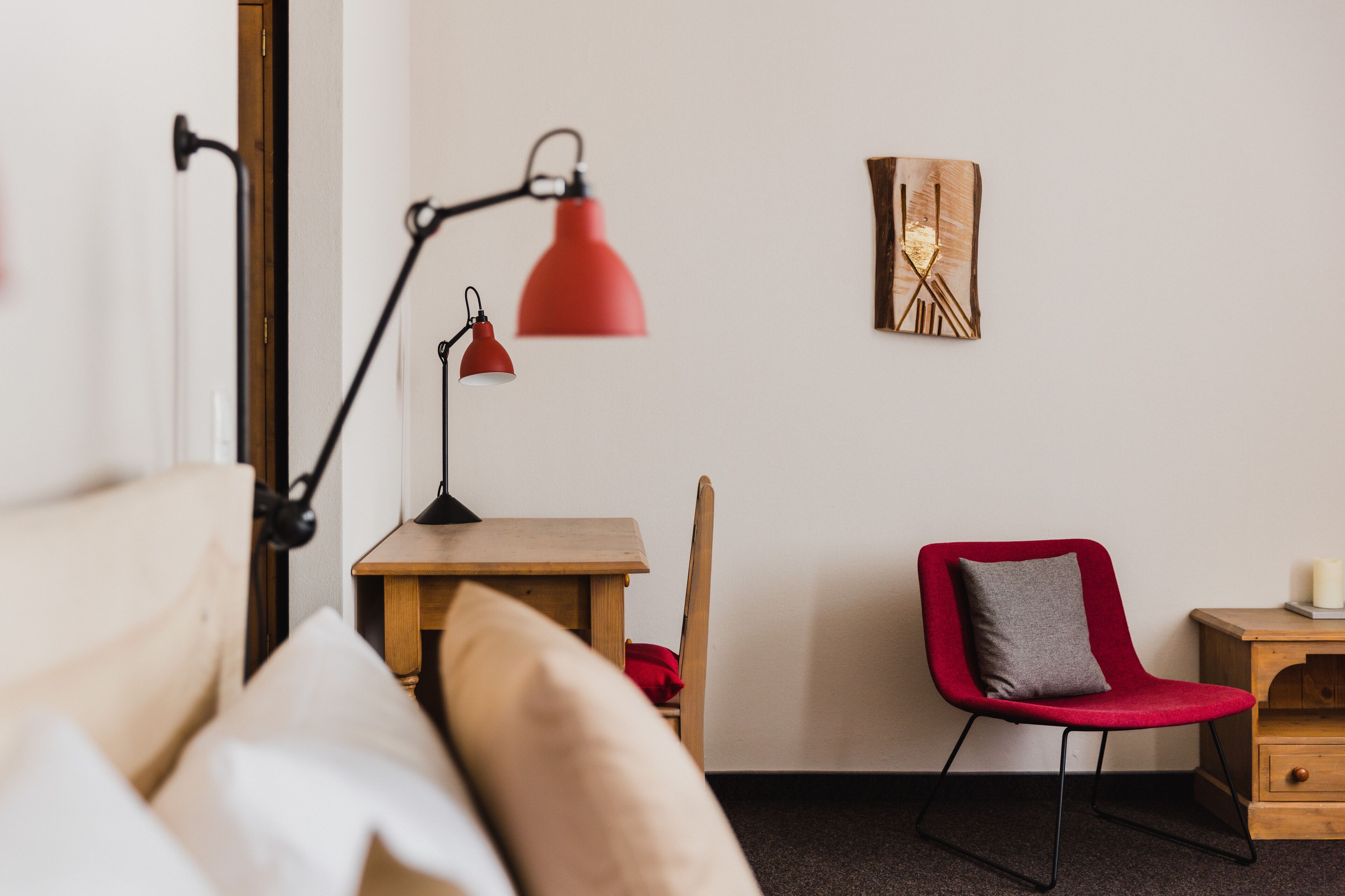 A neatly arranged room with a bed, a desk, a chair, a lamp, and a wall-mounted artwork.