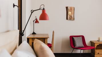 A neatly arranged room with a bed, a desk, a chair, a lamp, and a wall-mounted artwork.