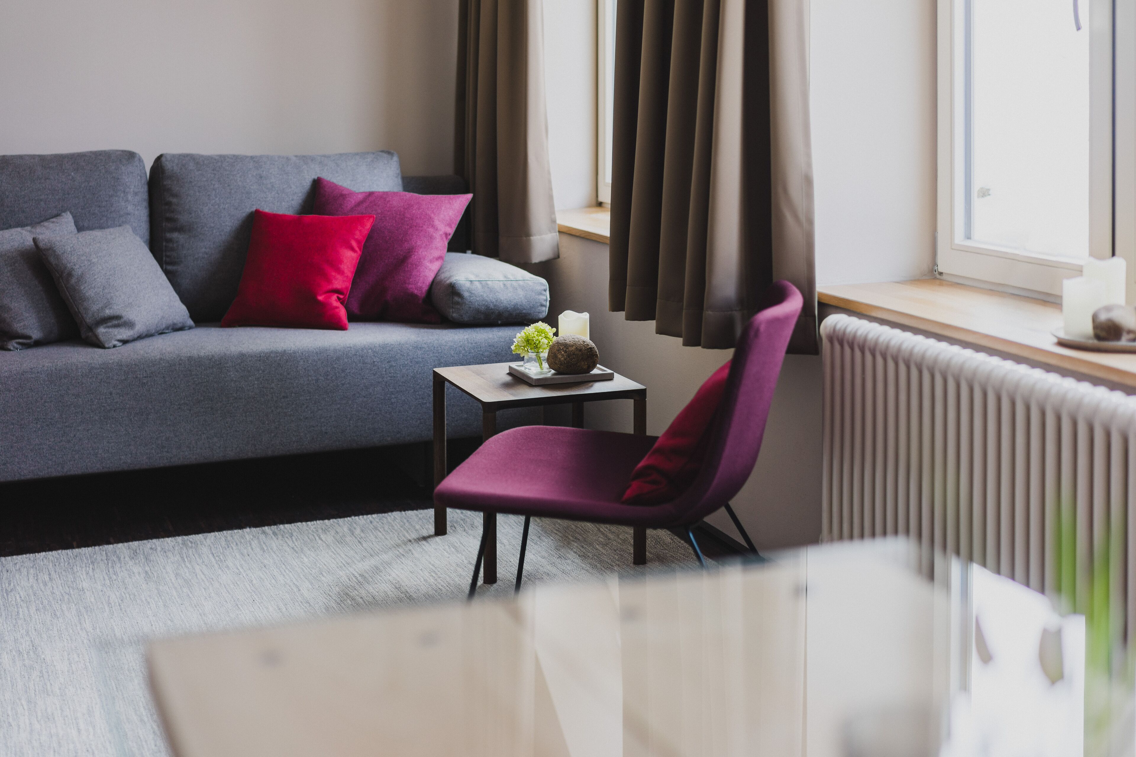 A modern living room with a grey sofa, a small table with a candle, and a purple chair.