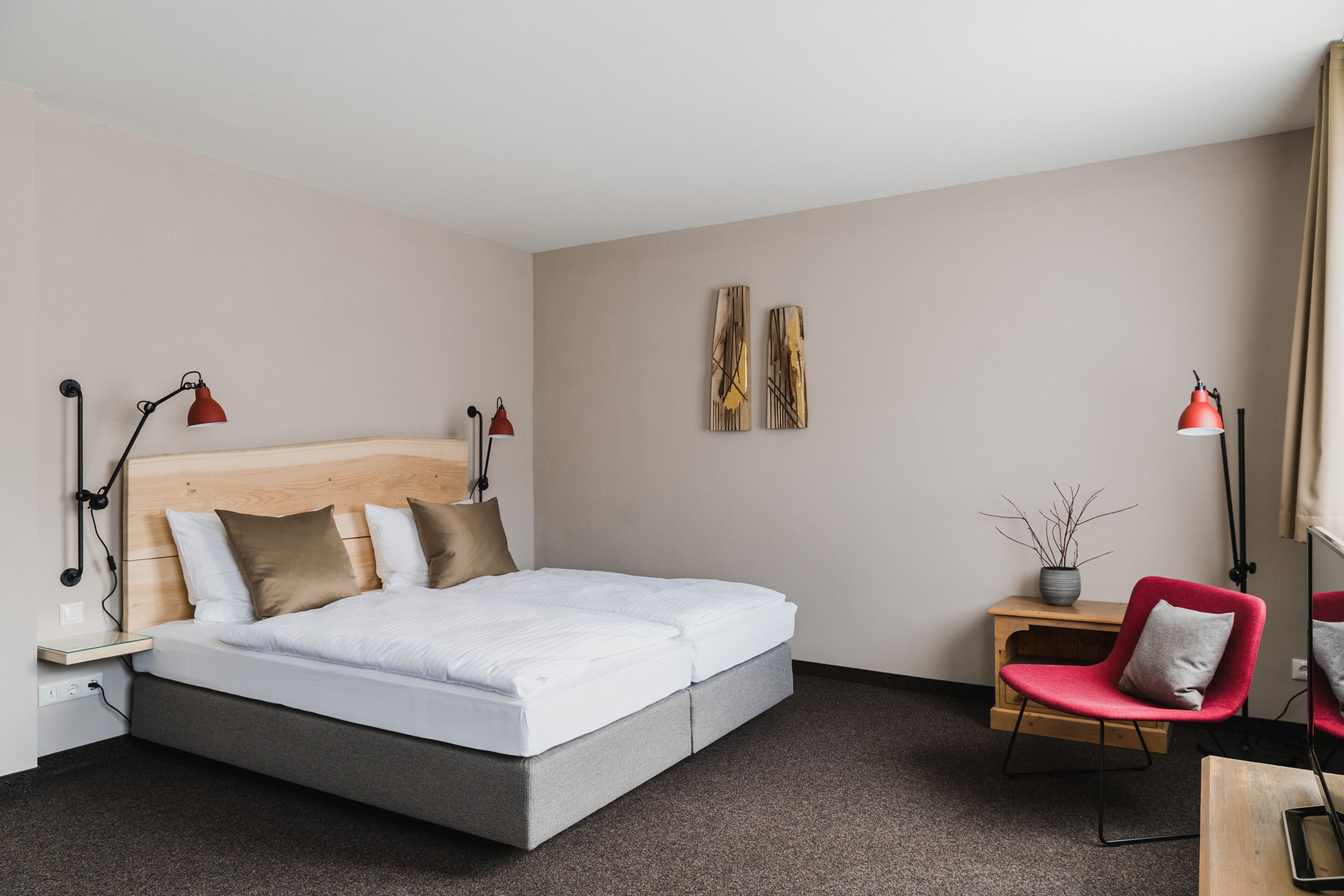 Ein modernes Hotelzimmer mit einem Bett mit Holz-Kopfteil, einem kleinen Schreibtisch mit Stuhl und zwei Wandlampen.