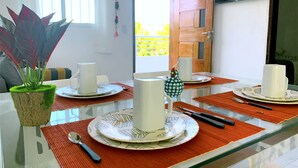 A dining area with a glass table, red placemats, white plates with leaf patterns, and a potted plant. - RENT apartments in Porto de Galinhas, fully equipped and new! (Porto de Galinhas)