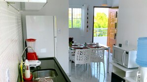 A modern kitchen with a gas stove, a microwave, and a water dispenser. There is a dining area with a table and chairs. - RENT apartments in Porto de Galinhas, fully equipped and new! (Porto de Galinhas)