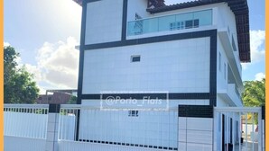 A modern two-story building with a white facade and dark trim, featuring a balcony on the upper floor. - RENT apartments in Porto de Galinhas, fully equipped and new! (Porto de Galinhas)