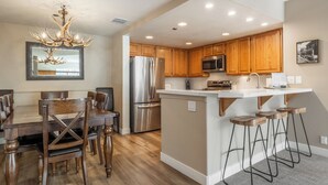 A modern kitchen with wooden cabinets, stainless steel appliances, and a bar stool area.