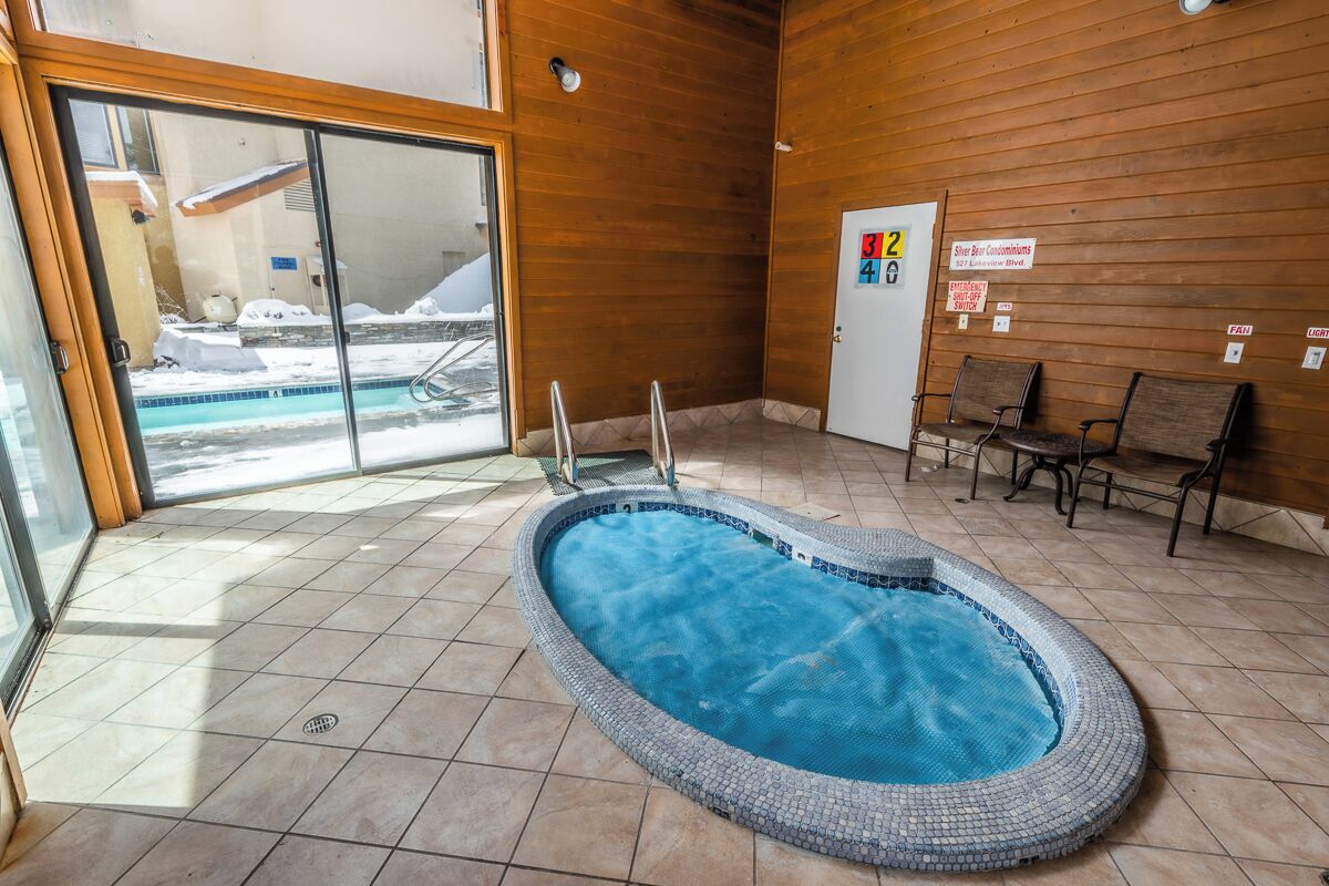 A small indoor pool with a tiled floor and a wooden wall. There are two chairs and a door with a sign above it.