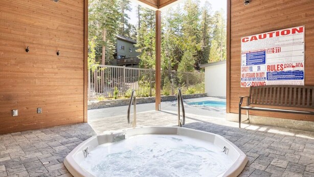 A hot tub area with a wooden interior, a pool, and a caution sign.